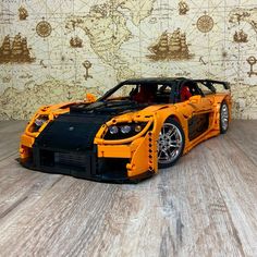 an orange lego car sitting on top of a wooden table next to a wall with a map