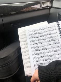 someone is holding a sheet of music in their hand while sitting in the driver's seat of a car