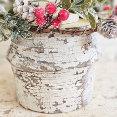 a white pot with holly, berries and pine cones