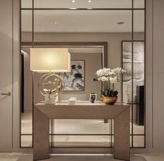 a modern console table with vases and flowers on it in front of a mirror