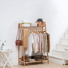 a clothes rack with clothing hanging on it in front of a white wall and stairs