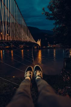 someone's feet are standing in front of a bridge at night