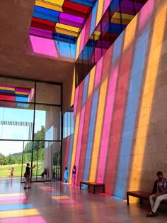 people are sitting on benches in an open room with colorful walls and floor coverings