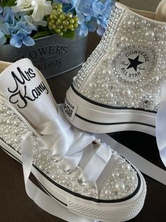 two pairs of white converse high top sneakers with pearls and bows on the side, sitting next to each other