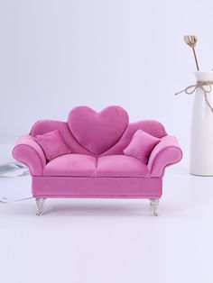 a pink love seat next to a white vase with a heart shaped pillow on it