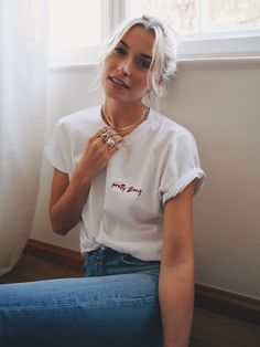 a woman sitting in front of a window wearing a white shirt with merry lettering on it