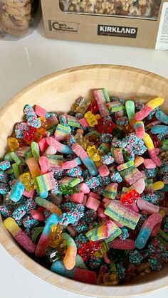 a wooden bowl filled with lots of colorful gummy bears next to a box of krispy kreme cereal