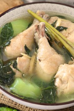 a white bowl filled with chicken and greens on top of a wooden table next to bread