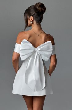 the back of a woman's white dress with a large bow on her shoulder