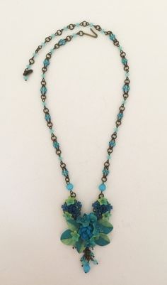 We call this color Azure with deep shades of teal, shaded with soft aqua mixed together. This is a smaller necklace beaded with glass beads and hand painted resin flowers. The central motif measures 1.5 inches across with a deep turquoise blue rose and is flanked on either side with drops that are 1.5 inches long. The chain is also handbeaded. This piece is great for someone who likes a smaller more delicate necklace. Lovely color for the beach. There are two matching earrings available for this Blue Single Strand Czech Glass Necklace, Blue Flower-shaped Beaded Necklace Gift, Blue Flower-shaped Beaded Necklaces, Elegant Blue Flower-shaped Necklace, Unique Flower-shaped Colorful Beaded Necklaces, Small Necklace, Shades Of Teal, Blue Pendant, Azure Blue