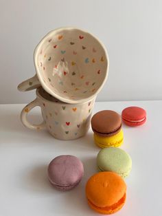 three different colored macaroons sitting next to a coffee cup on a white table