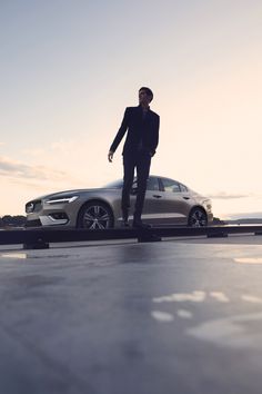 a man in a suit standing next to a silver car