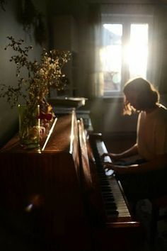 a woman sitting at a piano in front of a window with sunlight streaming through it