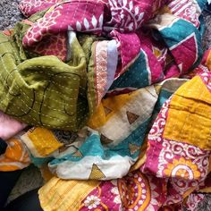 a pile of colorful scarves sitting on top of a floor next to a person