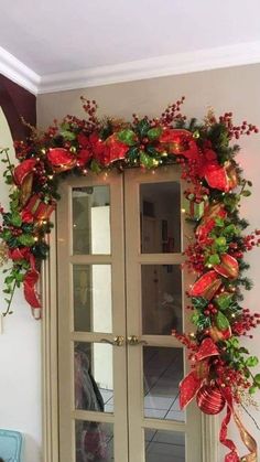 a door decorated with red and green christmas wreaths, holly berries, bows and lights