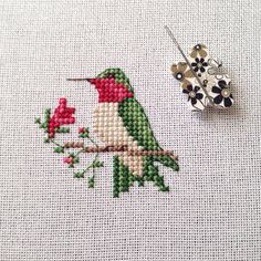 a cross stitch pattern with a bird and flower on the side, next to it is a brooch pin