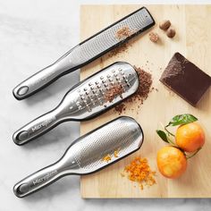 three kitchen utensils sitting on top of a cutting board next to fruit and chocolate