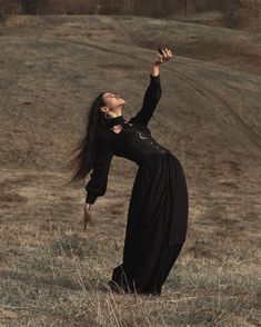 a woman in a black dress is holding her hand up to the sky while standing in a field