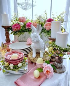 a table topped with plates and vases filled with flowers next to a bunny figurine