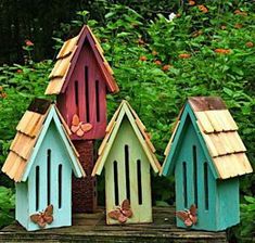 three birdhouses are sitting on a log in the grass and bushes, with butterflies flying around them