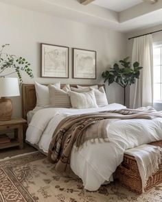 a large bed with white sheets and pillows in a bedroom next to a window filled with potted plants