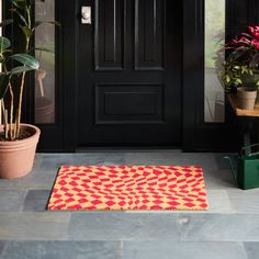 a red and yellow door mat sitting on top of a stone floor next to potted plants