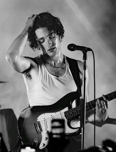 a man with curly hair playing guitar in front of a microphone