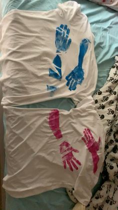 two shirts with handprints on them laying on a bed