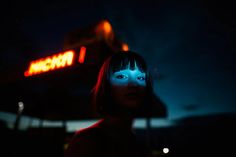 a woman standing in front of a neon sign at night with blue light on her face