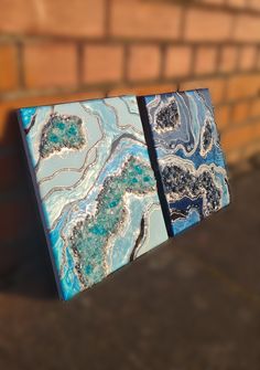 two blue and white abstract paintings hanging on a brick wall