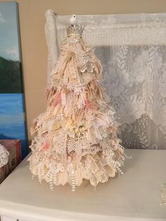 a white table topped with a small christmas tree next to a window covered in lace