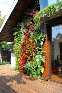 an outdoor living area with plants and flowers on the side of the house that is covered in wood planks