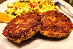 two crab cakes on a plate with corn and salad