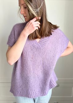 a woman wearing a purple sweater and blue jeans is standing in front of a white wall