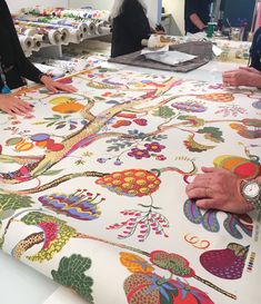 two people standing at a table covered in colorful fabric with flowers and birds on it