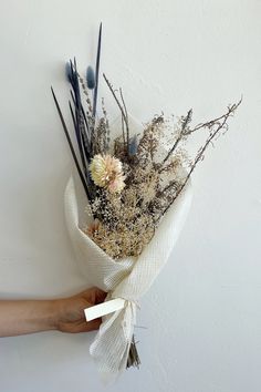 a hand holding a bouquet of dried flowers on a white wall with the stems still attached to it