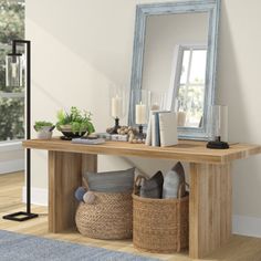 a wooden table with baskets and candles on it in front of a large mirror, next to a floor lamp