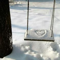 a swing hanging from a tree in the snow with a heart drawn on it's side