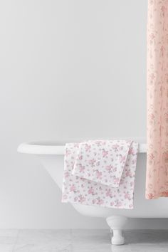 a white bath tub sitting next to a shower curtain with pink flowers on the bottom