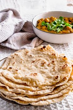 several flat breads on a plate next to a bowl of curry and a white towel