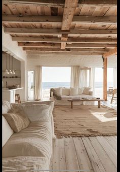 a living room with white furniture and wooden beams on the ceiling, along with an ocean view