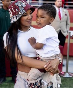 a woman holding a child in her arms at a football game with other people watching