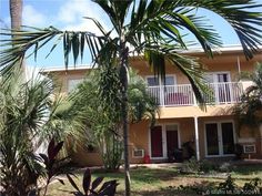 a palm tree in front of a yellow building with red doors and balconies