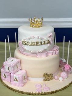 a three tiered cake is decorated with pink and gold decorations, including baby blocks