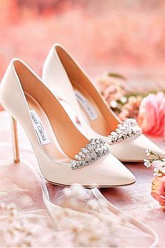 a pair of white high heel shoes sitting on top of a table next to flowers