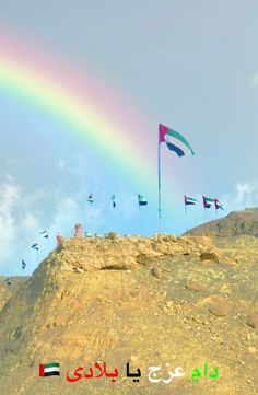 there is a rainbow in the sky and many flags are flying on top of this hill