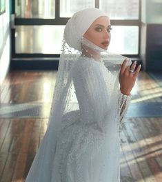 a woman in a white dress and veil standing on a hard wood floor with her hand up to her face