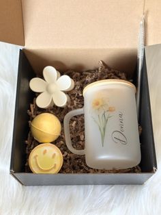 an open box containing a coffee mug, cookie and flowers