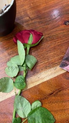 a single red rose sitting on top of a wooden table next to a book and pen