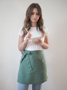 a woman wearing a green skirt and holding a pen in her hand while standing against a white wall